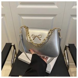 Detail of silver metallic bag featuring a gold bow buckle and elegant dual chain straps