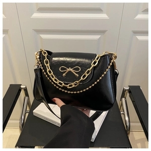 Detail of black patent leather shoulder bag with gold bow clasp and metallic chain straps