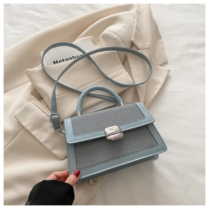 Dettaglio borsa a mano azzurra intrecciata con chiusura a scatto su sfondo di un blazer