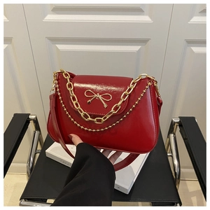 Detail of red patent leather bag with gold bow ornament and metallic chain straps