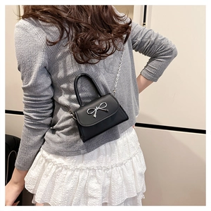 Détail d'un petit sac carré noir avec noeud métallique argenté et bandoulière chaîne