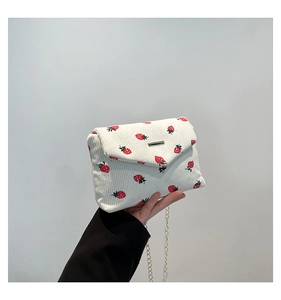 Detail of white corduroy shoulder bag featuring red strawberry prints and gold chain
