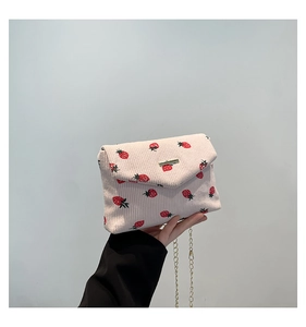 Detail of strawberry print corduroy handbag with gold chain strap and metal buckle