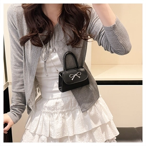 Close-up of black leather handbag featuring a silver metal bow buckle and chain strap