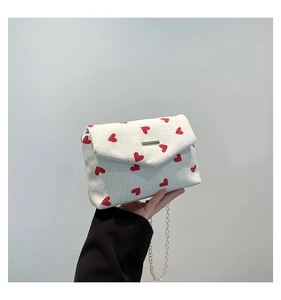 Detailed shot of white corduroy chain bag featuring red heart prints and gold metal buckle