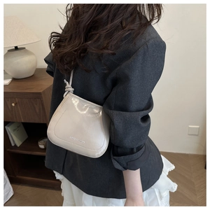 Detail of cream-colored glossy saddle bag with metal lettering and knotted strap