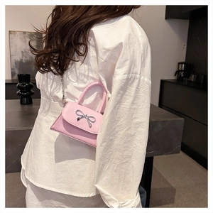 Pink crossbody bag with a silver bow detail shown on a model wearing white outfit