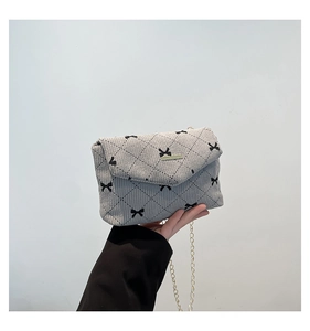 Detail of grey corduroy crossbody bag featuring black bow print and gold chain strap