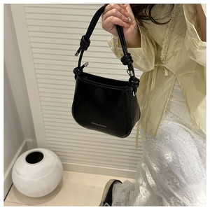 Detail of black leather underarm bag with thin knotted handles and metal hardware