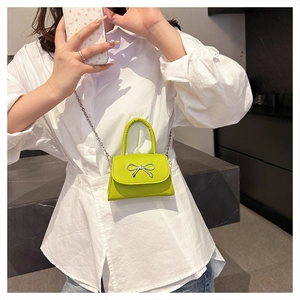 Détail d'un sac bandoulière vert fluo avec nœud argenté sur une tenue chemise blanche