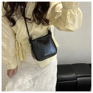 Detail of black PU leather crossbody bag with knot shoulder strap on lace dress