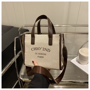 Detail of canvas tote bag with brown leather trim and chic brand logo lettering