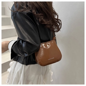 Side view of a glossy brown saddle bag on a model wearing a black leather jacket