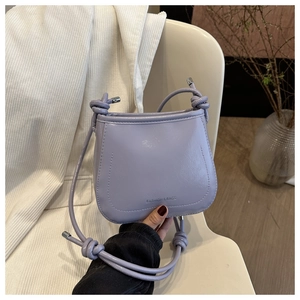 Detail of lilac matte leather crossbody bag with knot strap on a white chair