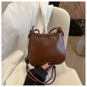 Detail of a brown vintage leather crossbody bag with silver lettering and metallic knots