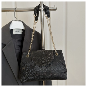 Detail of black faux snake skin texture and gold chain on luxury shoulder bag