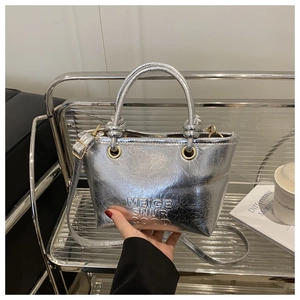 Detailed macro view of the silver metallic bucket bag with embossed lettering on the shelf