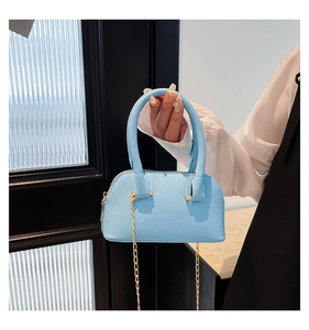 Close-up of sky blue litchi pattern shell bag with golden chain held by model