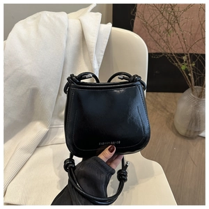 Detail of minimalist black glossy leather crossbody bag with silver printed logo text