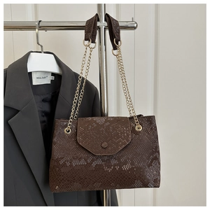Detail of dark brown snakeskin embossed handbag with gold chain strap on grey blazer