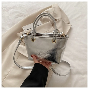 Close-up of silver metallic bucket bag featuring embossed text and golden metal ring detail