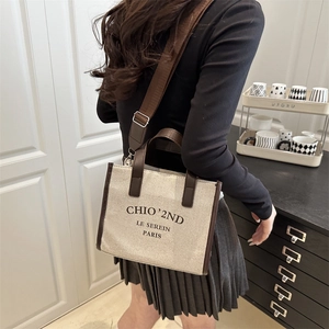 Beige canvas tote bag with brown leather trim and shoulder strap shown in a lifestyle setting