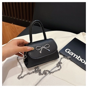 Détail d'un mini sac noir avec nœud argenté et bandoulière en chaîne métallique fine