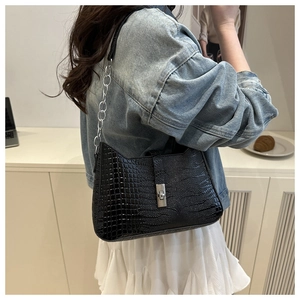 Detail of black crocodile texture handbag with silver chain strap shown on shoulder