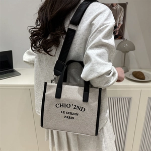 Minimalist canvas tote bag with black leather trim and adjustable strap in a lifestyle setting