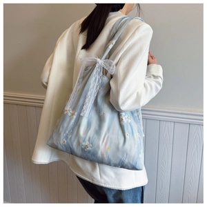 Close-up of light blue floral tote bag featuring white embroidery and lace bow detail