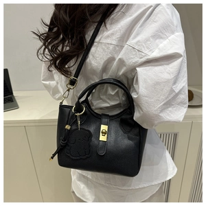 Detail of black lychee leather bucket bag with gold lock and bear charm accessory
