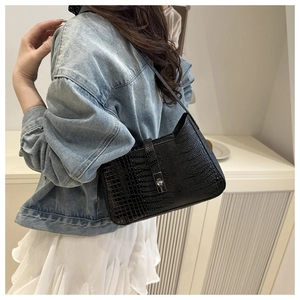 Detail of black crocodile texture handbag with silver metal lock on model shoulder
