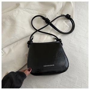 Detail of black glossy leather crossbody bag with knot strap and metallic logo lettering