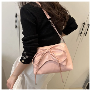 Détail d'un sac à bandoulière rose avec un grand nœud décoratif et une chaîne en métal