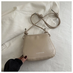 Detailed close-up of a light beige crossbody bag with knotted rope strap and metal tips