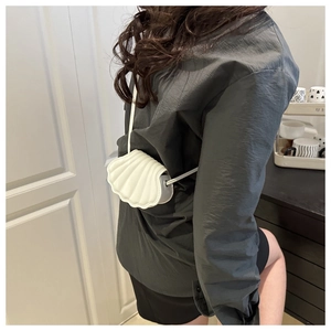 Detail of a white shell-shaped crossbody bag with vertical quilted texture and thin strap