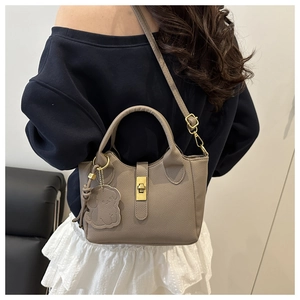 Detail view of taupe lychee leather bucket bag with dog charm and metal twist lock