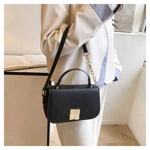 Détail du sac bandoulière en cuir noir avec boucle dorée et bandoulière chaîne sur modèle
