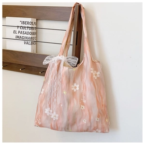 Detail of pink tie-dye tote bag with floral embroidery and a large lace bow