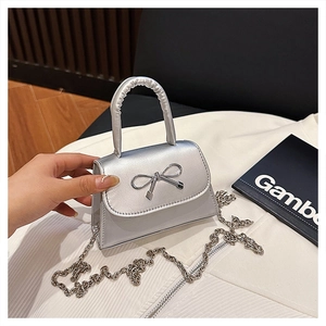 Détail de mini sac argenté avec nœud métallique décoratif et texture cuir synthétique