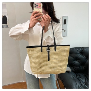 Detail of a large straw tote bag featuring black leather handles and woven texture finish