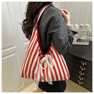 Detail of red striped canvas tote bag featuring a white lace bow and handmade metal plate