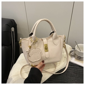Détail du sac seau crème avec texture grainée, fermoir doré et breloque chien
