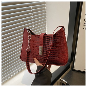 Detail of deep red crocodile pattern leather bag featuring a silver metal twist lock