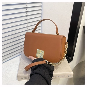 Vue détaillée du sac en cuir marron avec boucle dorée et chaîne sur des livres