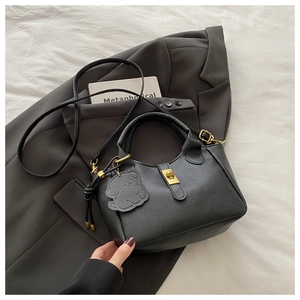 Detail of black litchi grain leather bucket bag with gold lock and bear charm accessory