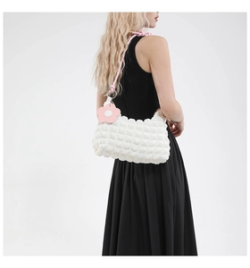 Close-up of white pleated cloud bag featuring pink braided strap and floral pendant