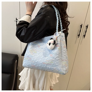 Detail of light blue tote bag with textured patterns and a cute panda plush charm
