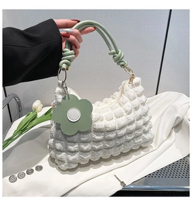 Detail of white bubble texture fabric bag with green knotted handle and flower charm