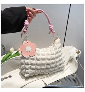 Close-up of white bubble quilted bag with pink knotted handle and floral charm
